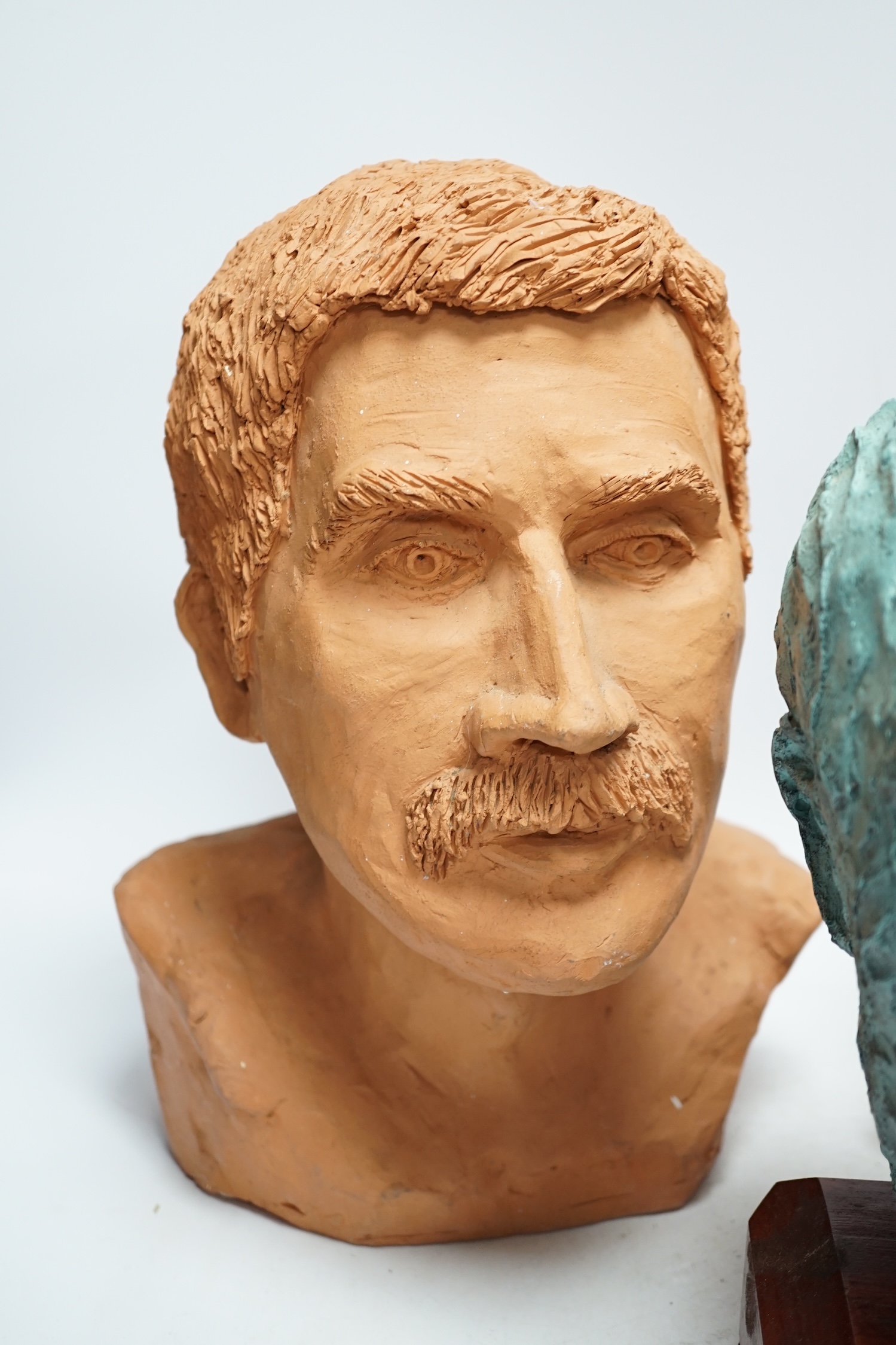 Four art pottery sculpted heads on stands, two terracotta and two painted verdigris green, largest 34cm high